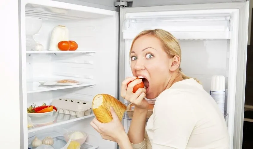 A woman eating from the refrigerator