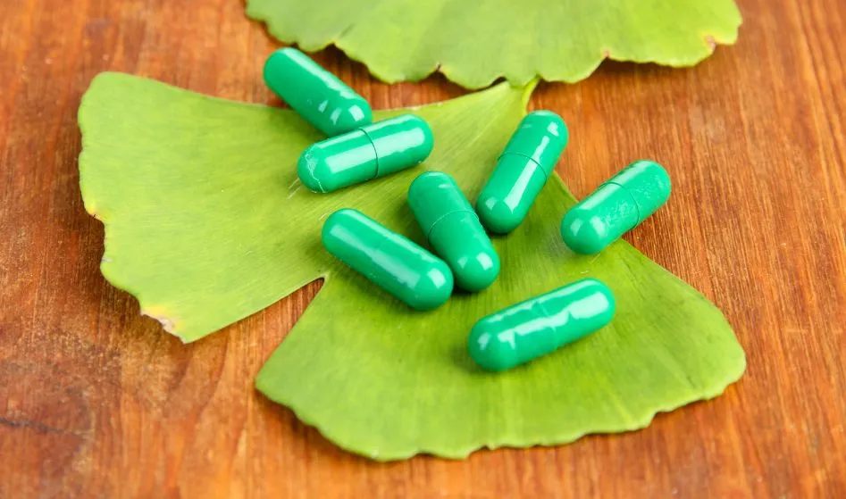 Ginkgo biloba leaves and pills on wooden background